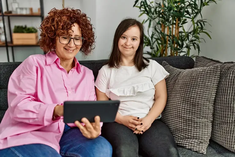 Mature mother and down syndrome daughter at home using touchpad device