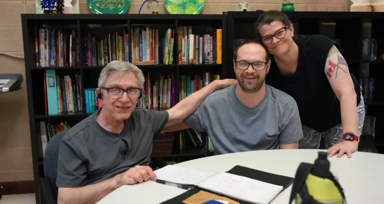 individuals sitting at a table smiling with a bookcase in the background